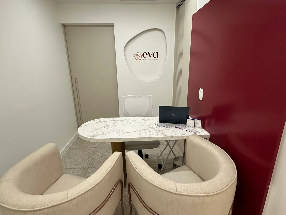 Recepção da clínica Eva com mesa em mármore, cadeiras estofadas e painel acolhedor